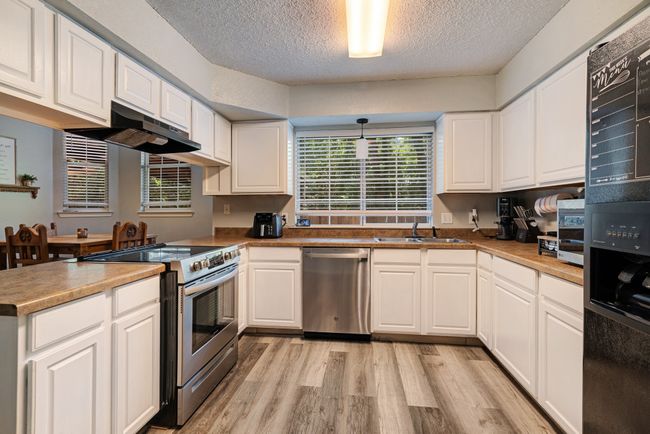 Kitchen featuring stainless steel appliances, light wood-style flooring, white cabinets, a textured ceiling, and under cabinet range hood | Image 7