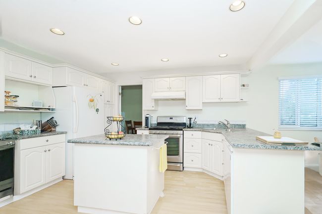 Kitchen featuring stainless steel gas range oven, open shelves, freestanding refrigerator, a peninsula, and light stone counters | Image 8