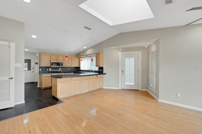 Kitchen featuring light brown cabinets, hardwood / wood-style floors, stainless steel appliances, dark countertops, and lofted ceiling with skylight | Image 20