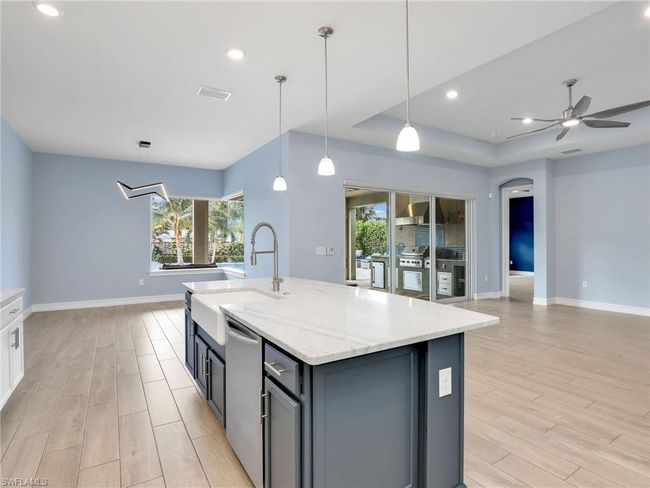 Kitchen with light wood-type flooring, decorative light fixtures, light stone counters, and a center island with sink | Image 16