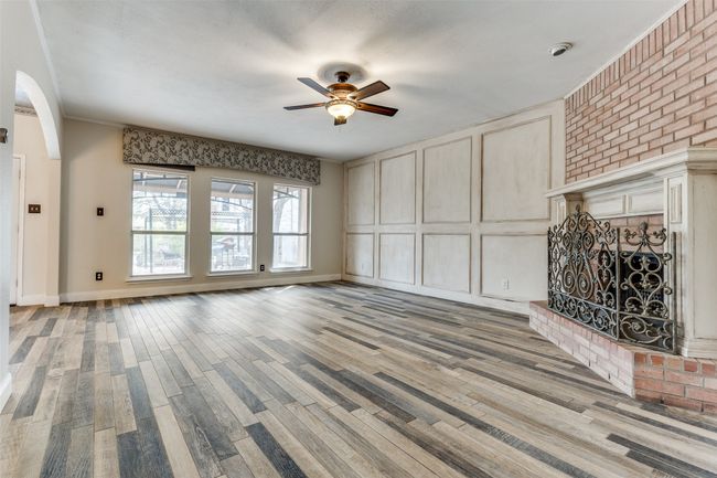 Unfurnished living room with light wood finished floors, a brick fireplace, ceiling fan, arched walkways, and a decorative wall | Image 8