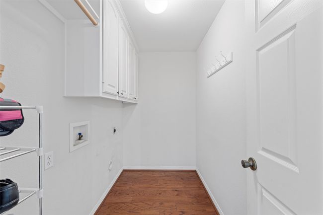 Laundry area with hookup for a washing machine, baseboards, wood finished floors, and cabinet space | Image 26