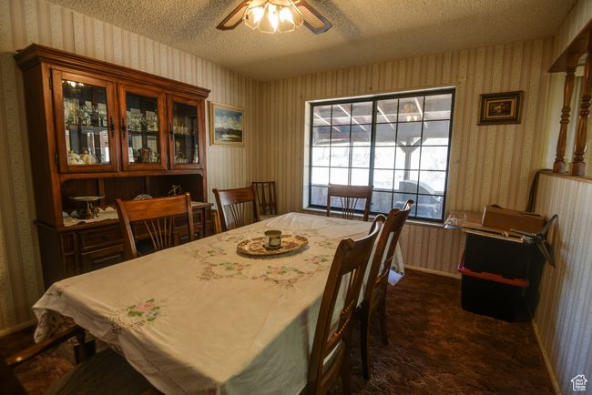Dining room featuring wallpapered walls, a textured ceiling, a ceiling fan, and dark carpet | Image 31
