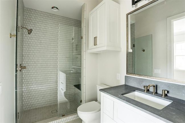 This beautifully designed en-suite showcases a glass-enclosed shower with a built-in bench and elegant mosaic stone surround. A sleek quartz vanity, custom cabinetry, and a designer mirror complete the space with timeless style and sophistication. | Image 25