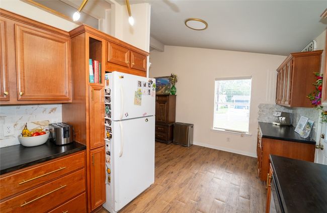 Kitchen featuring freestanding refrigerator, dark countertops, tasteful backsplash, light floors, and brown cabinetry | Image 13