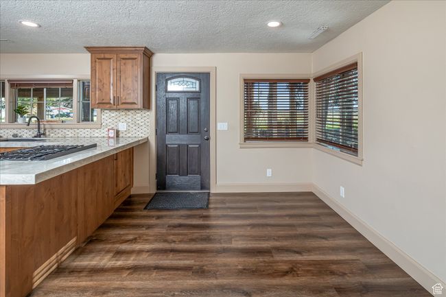 Kitchen featuring brown cabinets, dark wood-type flooring, a textured ceiling, decorative backsplash, and recessed lighting | Image 21
