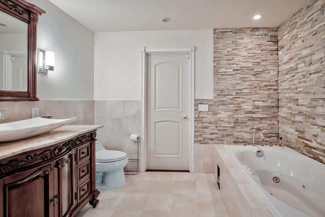 Full bath featuring toilet, a tub with jets, tile patterned flooring, vanity, and tile walls | Image 17