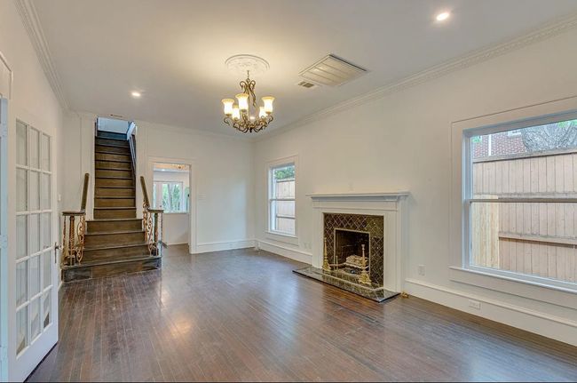Unfurnished living room featuring wood finished floors, crown molding, a chandelier, stairs, and a high end fireplace | Image 4