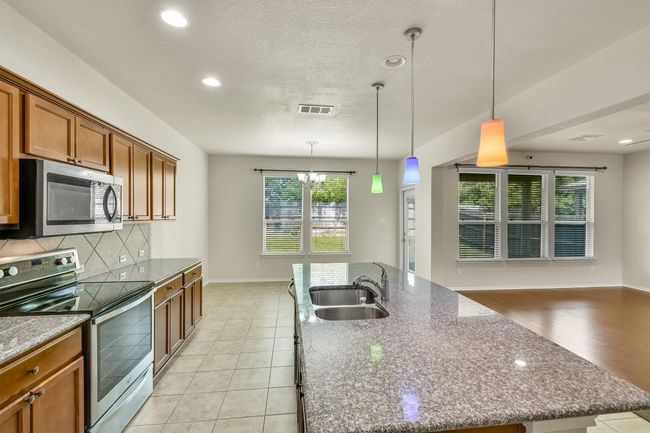 Kitchen with a kitchen island with sink, a sink, visible vents, brown cabinets, and appliances with stainless steel finishes | Image 11