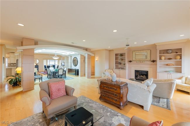 Living room with a fireplace, built-ins arched walkways, light wood-style flooring, and ornate columns | Image 14