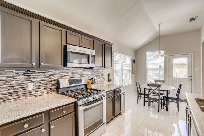 Kitchen with stainless steel appliances, decorative backsplash, vaulted ceiling, light tile patterned floors, and pendant lighting | Image 11