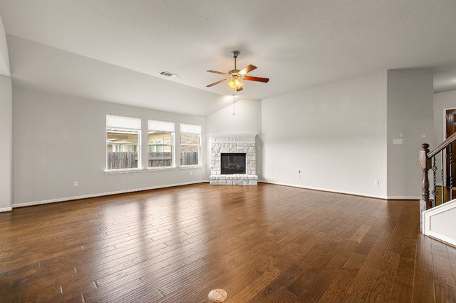Unfurnished living room featuring dark wood-style flooring, visible vents, stairs, ceiling fan, and a fireplace | Image 7