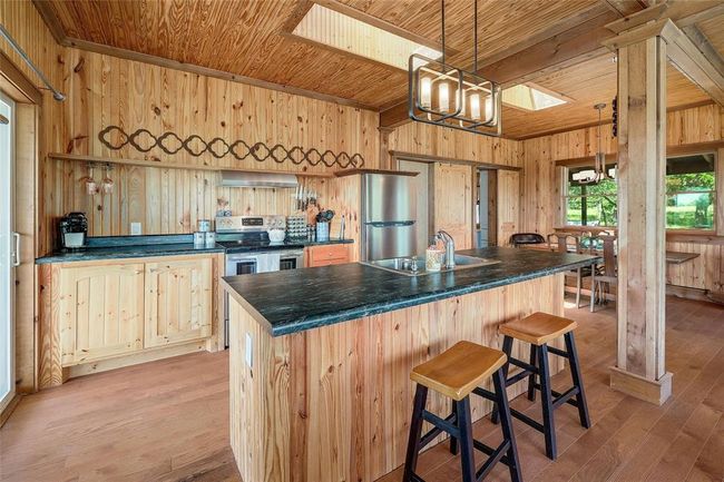 Kitchen featuring wall chimney range hood, a sink, wooden walls, wood ceiling, and stainless steel appliances | Image 15