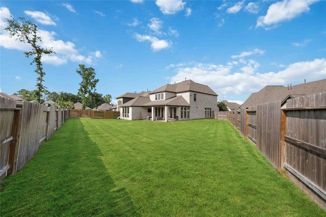 This photo showcases a spacious backyard with a well-maintained lawn, enclosed by a wooden fence. The house features a modern design with a large patio area, perfect for outdoor activities and entertaining. | Image 33