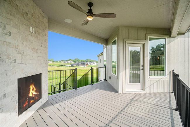 Wooden deck featuring a warm lit fireplace, ceiling fan, and a yard | Image 62