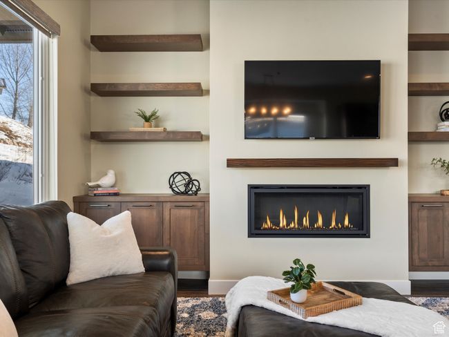 Living area with wood finished floors, a glass covered fireplace, built in features, and baseboards | Image 14
