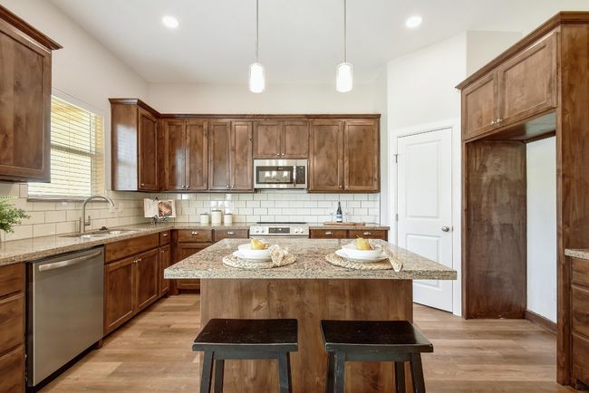 Kitchen featuring appliances with stainless steel finishes, light wood-type flooring, decorative backsplash, a center island, and decorative light fixtures | Image 9