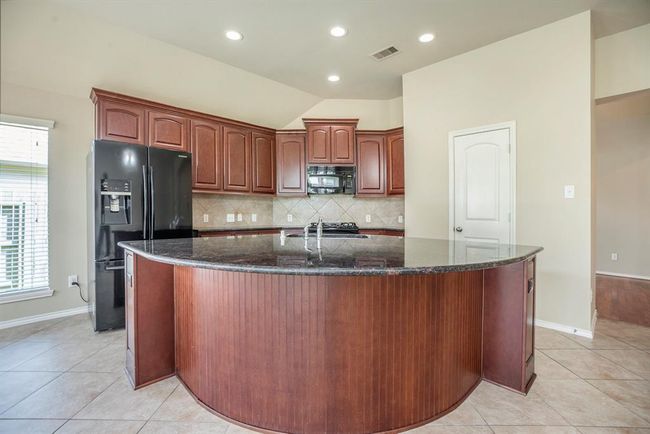 The spacious kitchen overlooks the living area and boasts rich wood cabinetry, granite countertops, a gas cooktop, and an oversized island with seating space—perfect for casual meals or morning coffee. Tile flooring throughout makes maintenance a breeze while keeping the space light and airy. | Image 11