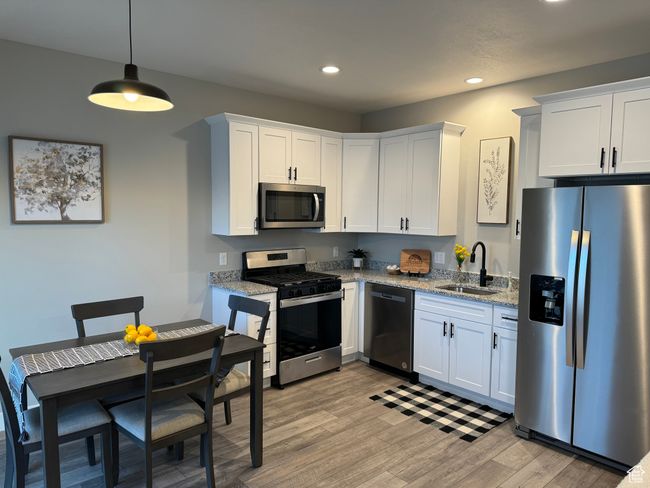 Kitchen featuring decorative light fixtures, appliances with stainless steel finishes, light hardwood / wood-style floors, sink, and white cabinets | Image 15