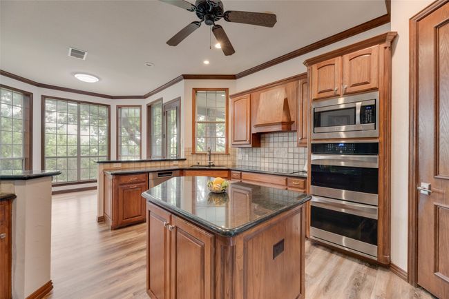 Kitchen with stainless steel appliances, light wood finished floors, crown molding, brown cabinets, and a peninsula | Image 7