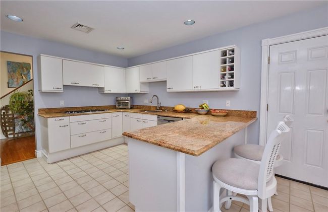 Kitchen with light tile patterned flooring, a kitchen bar, sink, stainless steel dishwasher, and kitchen peninsula | Image 22