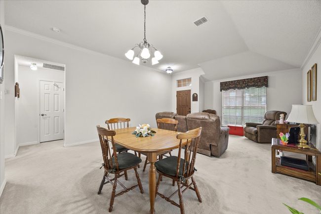 Dining area with light carpet, ornamental molding, and a chandelier | Image 9