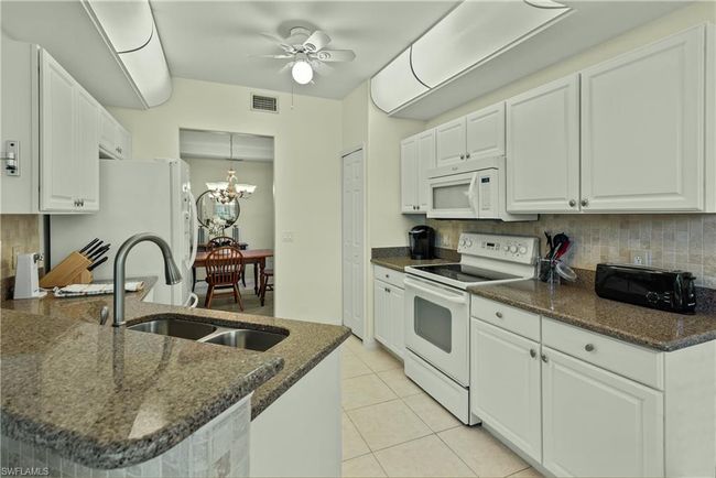 Kitchen with white cabinets, white appliances, dark stone countertops, and sink | Image 6