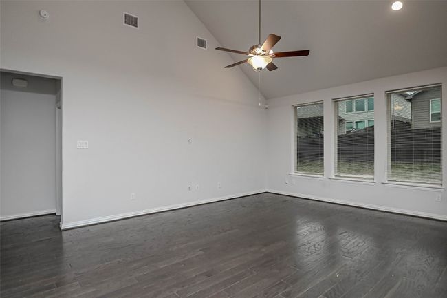 Empty room with dark wood-type flooring, high vaulted ceiling, visible vents, and a ceiling fan | Image 14
