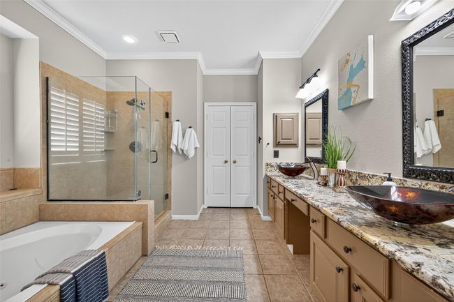 This spacious bathroom features a glass-enclosed shower, a large soaking tub, and a double vanity with elegant vessel sinks. The room is accented with neutral tiles and granite countertops, creating a modern and inviting atmosphere. | Image 29