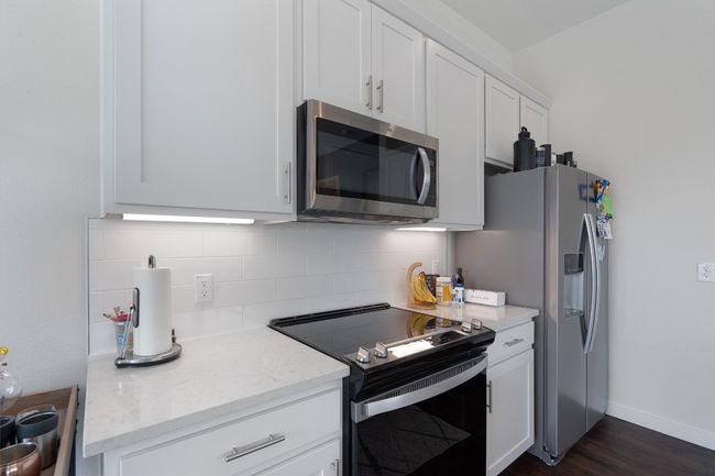 Kitchen featuring appliances with stainless steel finishes, decorative backsplash, white cabinets, dark wood-type flooring, and light stone countertops | Image 24