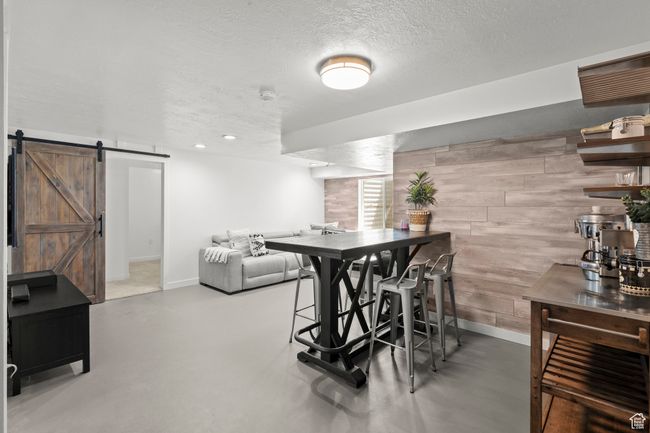 Dining area with wood walls, a textured ceiling, a barn door, finished concrete floors, and recessed lighting | Image 39