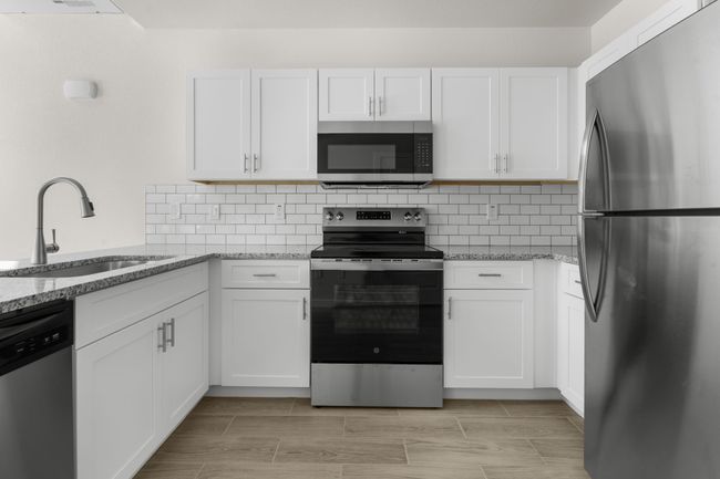 Kitchen with appliances with stainless steel finishes, white cabinetry, light stone countertops, and tasteful backsplash | Image 7