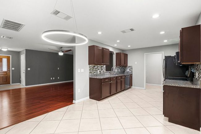 Kitchen featuring stainless steel dishwasher, decorative backsplash, ceiling fan, dark brown cabinets, and light wood finished floors | Image 9