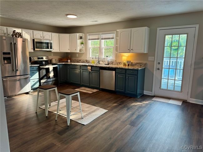 Kitchen with stainless steel appliances, a textured ceiling, white cabinetry, dark wood-style floors, and a sink | Image 5