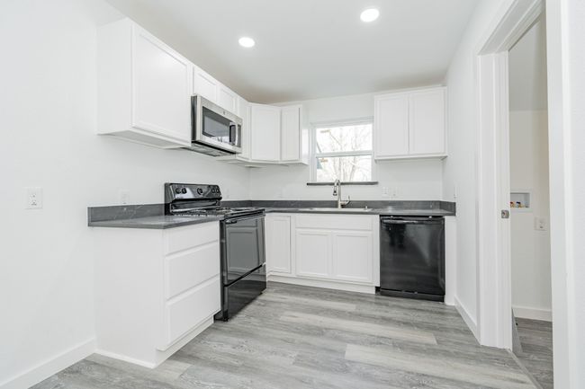Kitchen with dark countertops, black appliances, white cabinetry, and a sink | Image 7