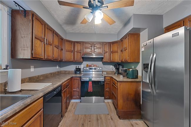 Kitchen featuring stainless steel appliances, under cabinet range hood, light wood-style flooring, brown cabinets, and a ceiling fan | Image 7