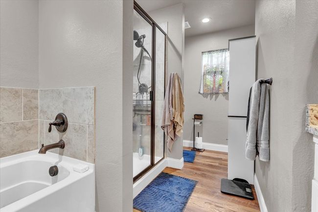 Bathroom with a garden tub, a stall shower, wood finished floors, and a textured wall | Image 16