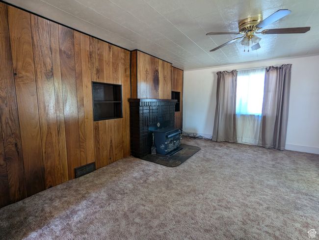 Unfurnished living room with carpet floors, a ceiling fan, wood walls, and a wood stove | Image 5