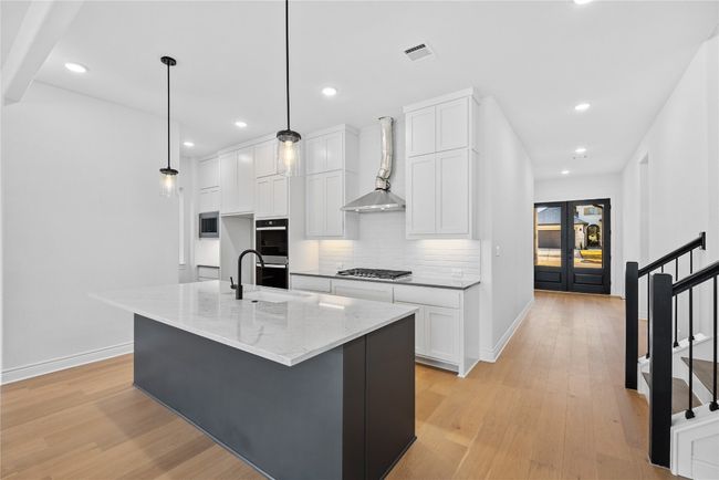 Kitchen with backsplash, white cabinets, light wood finished floors, light stone countertops, and wall chimney exhaust hood | Image 25