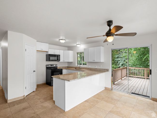 Kitchen featuring black appliances, a peninsula, ceiling fan, a sink, and white cabinets | Image 11