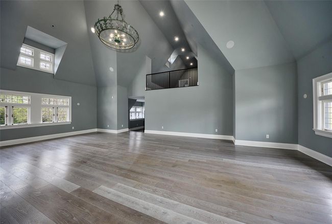 Unfurnished living room with an inviting chandelier, high vaulted ceiling, wood finished floors, and baseboards | Image 14