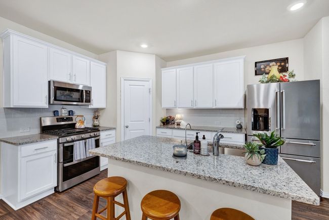 Kitchen with a breakfast bar, white cabinetry, backsplash, dark wood finished floors, and appliances with stainless steel finishes | Image 9