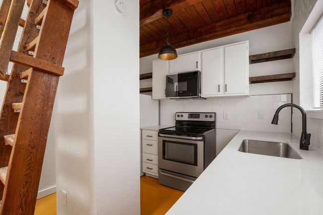 Kitchen featuring a sink, open shelves, black microwave, stainless steel range with electric stovetop, and decorative backsplash | Image 6