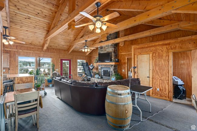 Carpeted living room featuring ceiling fan, wooden ceiling, a stone fireplace, lofted ceiling with beams, and wooden walls | Image 20