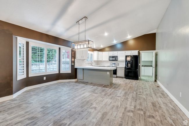 Kitchen featuring light wood finished floors, vaulted ceiling, backsplash, light countertops, and black appliances | Image 5