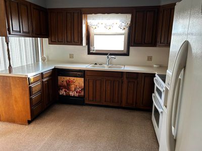 Kitchen featuring dark brown cabinets, light colored carpet, sink, and white appliances | Image 3