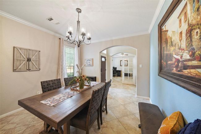 This dining area features a stylish chandelier. The room is well-lit with natural light from a large window, and it opens into a hallway with an arched entrance leading to additional living spaces. | Image 5