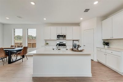 Kitchen with appliances with stainless steel finishes, white cabinets, a center island with sink, and light wood-type flooring | Image 3