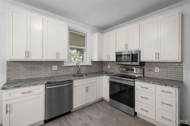 Kitchen with stainless steel appliances, decorative backsplash, light stone countertops, and light wood-style flooring | Image 10