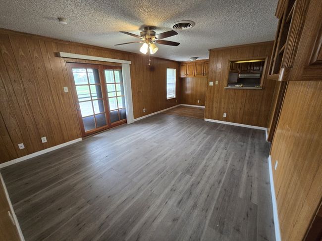 Unfurnished living room featuring a ceiling fan, wooden walls, dark wood-style flooring, and a textured ceiling | Image 13